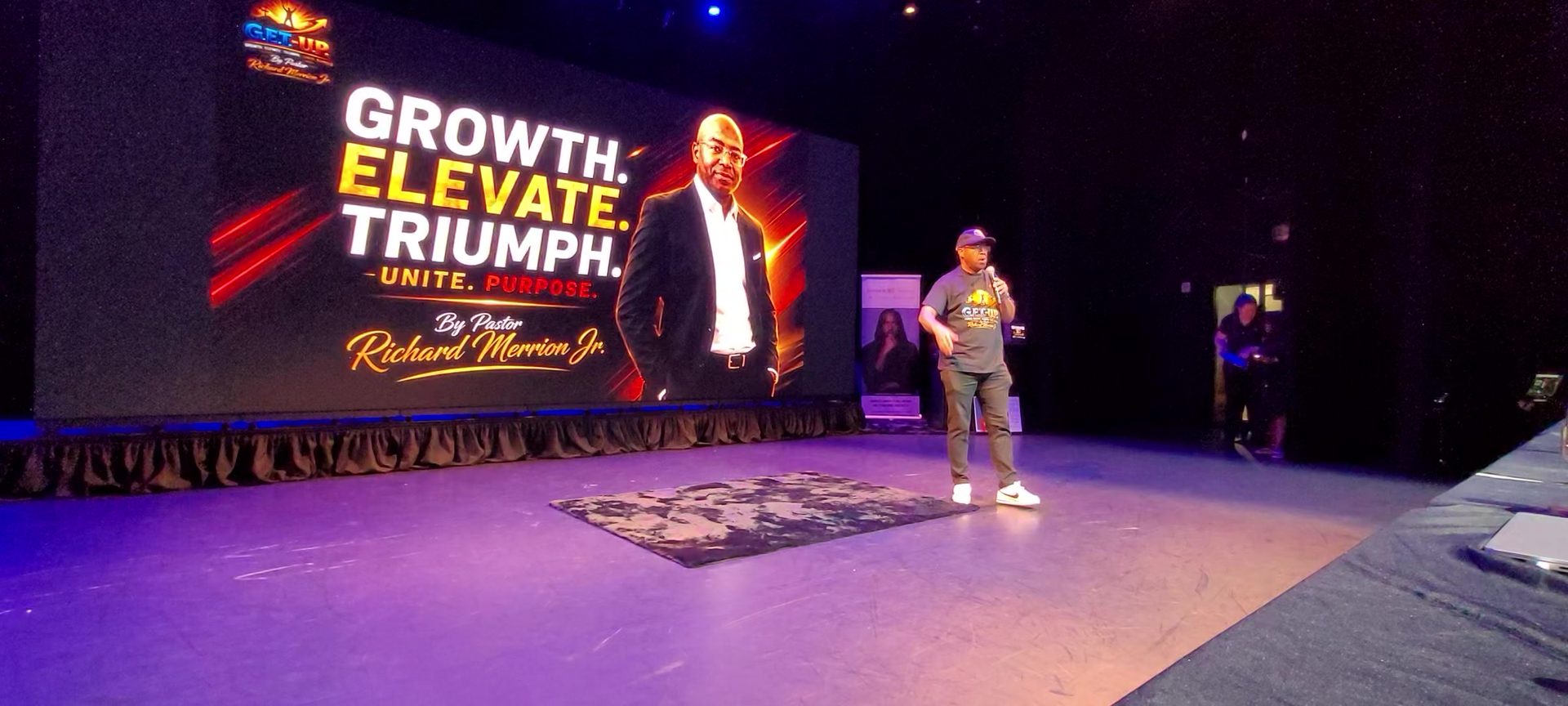 Pastor Richard Merrion Jr. speaking on stage in front of his G.E.T.-U.P. screen: Growth, Elevate, Triumph